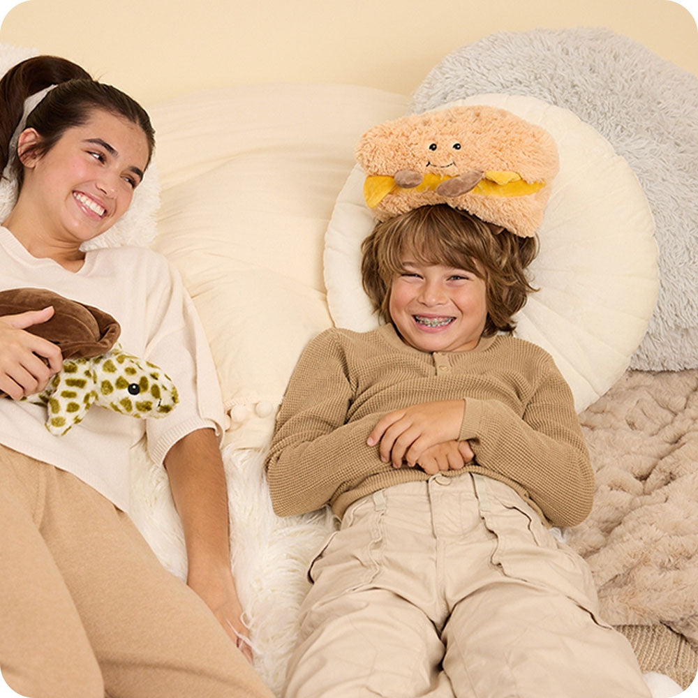Woman and child lying on a bed with plush toys, smiling.