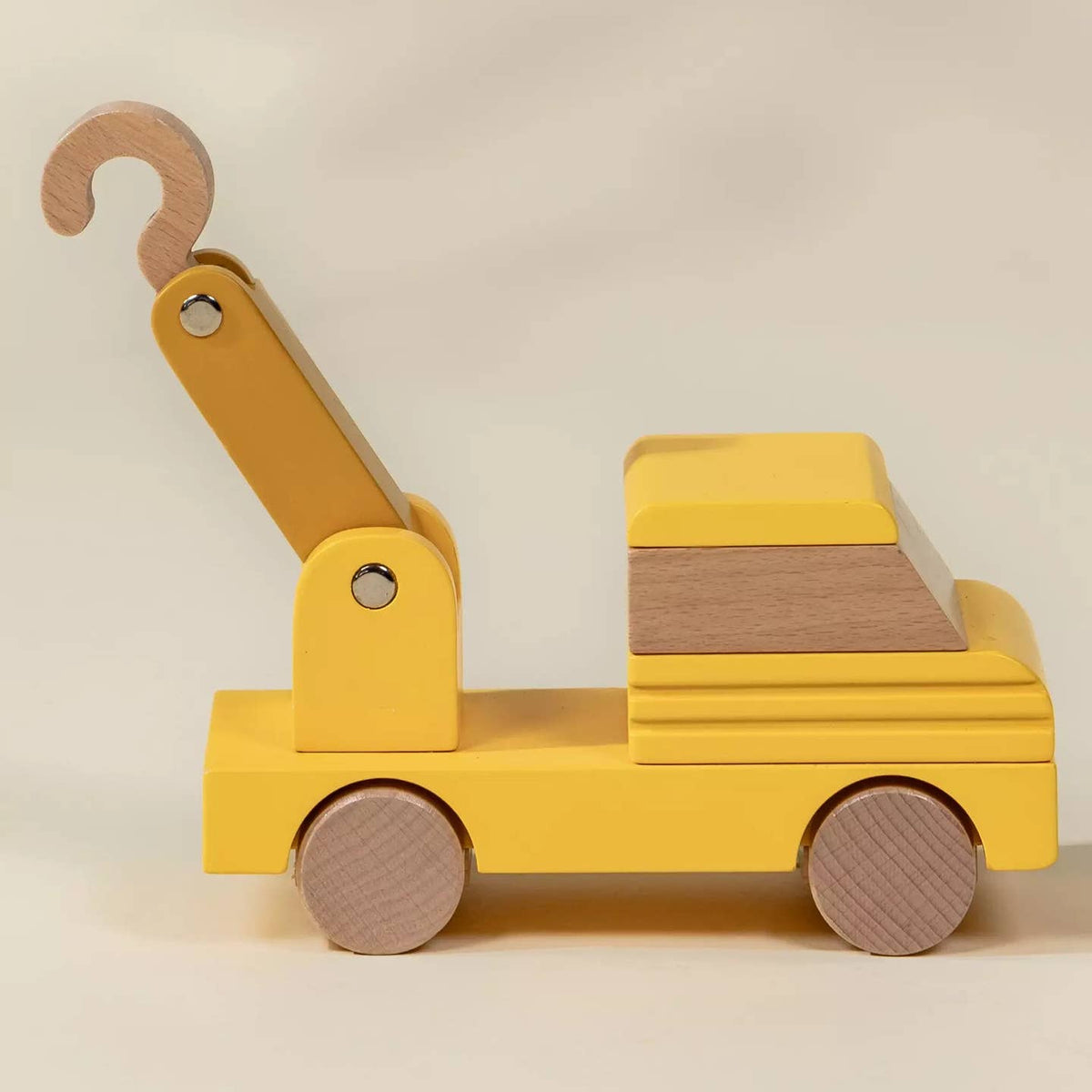 Wooden toy crane with yellow body and brown hook on a beige background