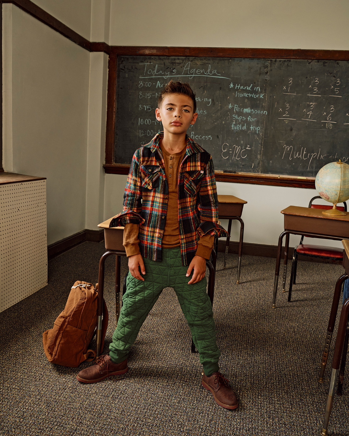Young boy standing in a classroom with a chalkboard in the background