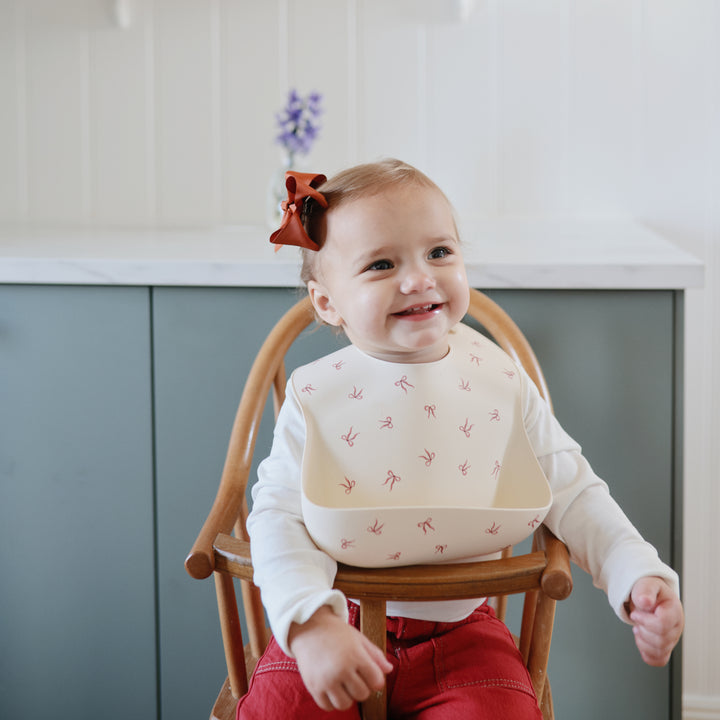 Baby sitting in a high chair wearing a bib with a floral pattern, smiling.