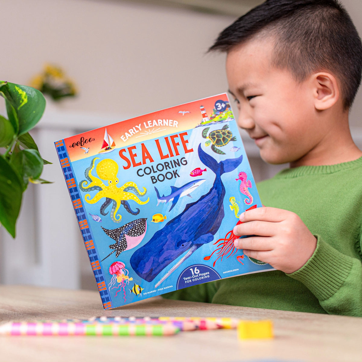 Child holding a 'Sea Life Coloring Book' with colorful illustrations on a table.