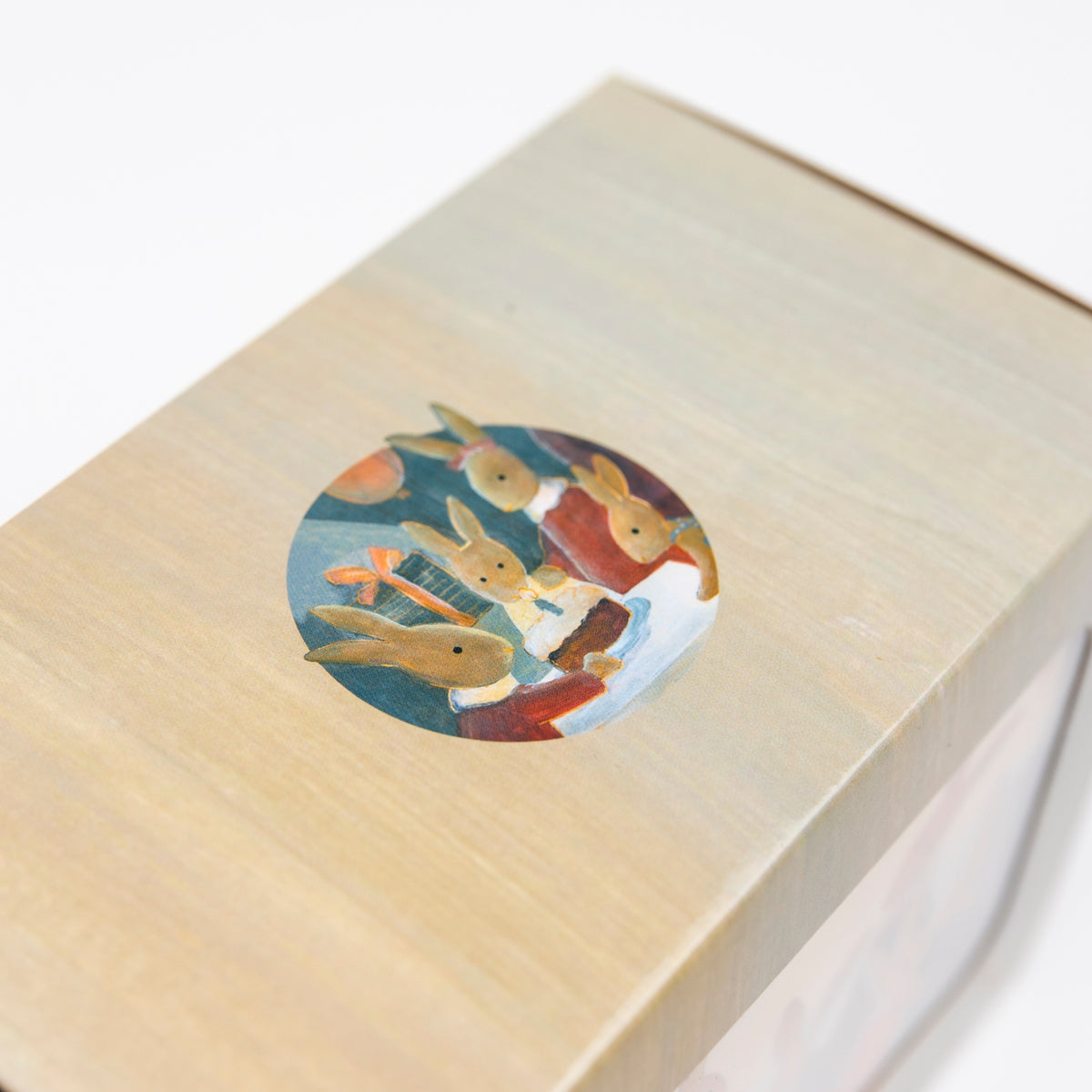 A close-up of a light wood box lid featuring a circular illustration of rabbits in colorful clothing, photographed against a clean white background.