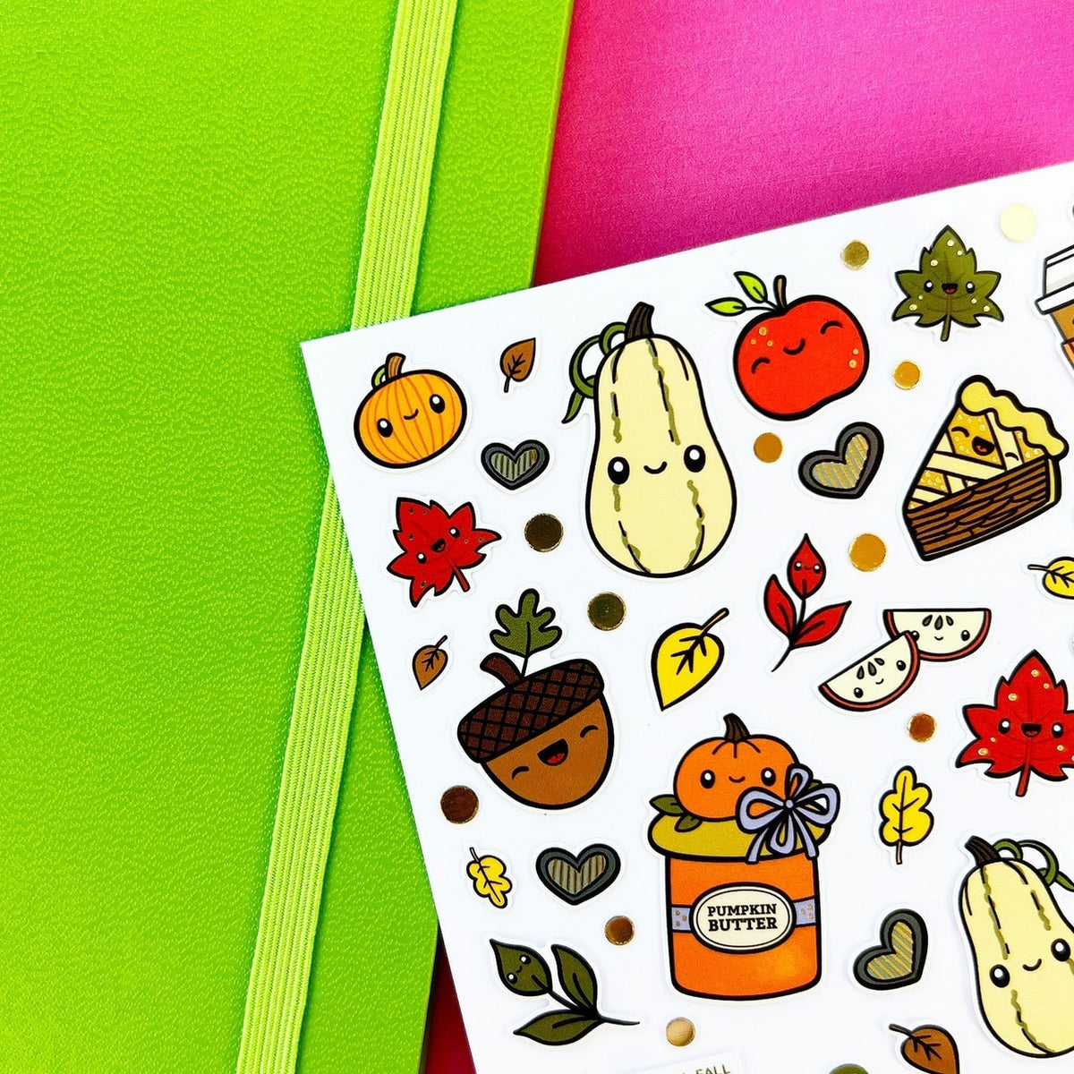 A sheet of autumn-themed stickers featuring cute cartoon illustrations of pumpkins, acorns, leaves, and pie slices on a white background, styled on top of bright green and pink paper sheets.