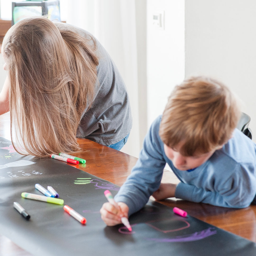 Woman and child drawing on a large piece of paper with markers.