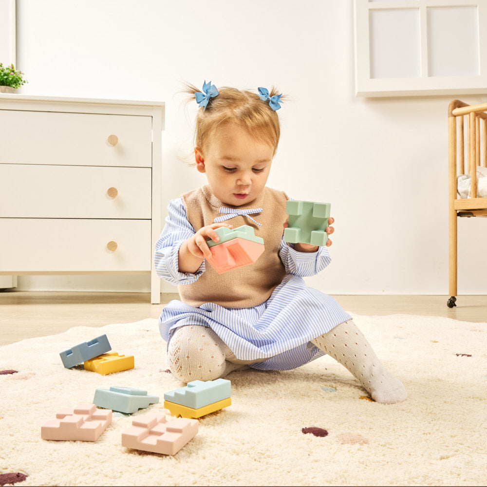 Child playing with colorful blocks on a carpeted floor in a room with furniture.