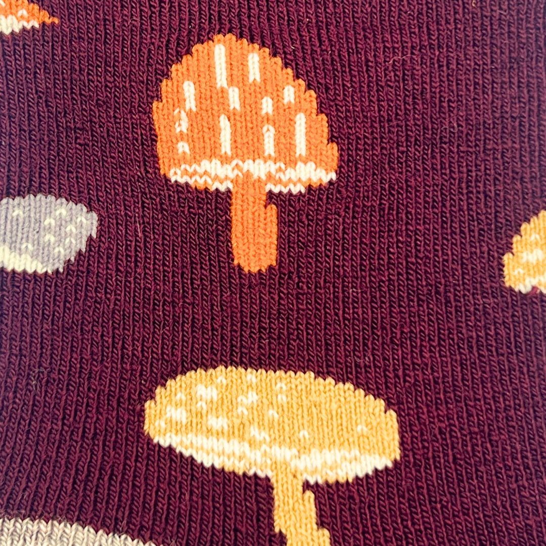 Close-up of a knit fabric with a burgundy background and a repeating mushroom pattern in orange, pale yellow, and light gray.