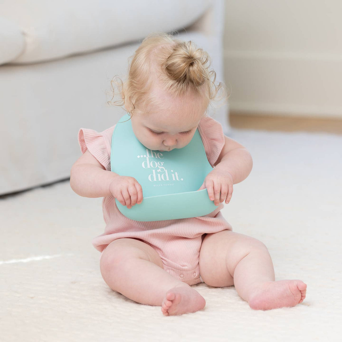 Baby wearing a light blue bib with text, sitting on a white surface.