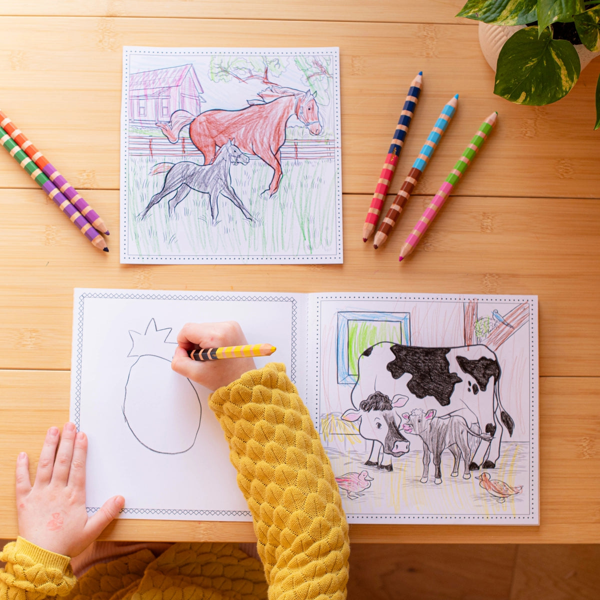 Coloring book with animal illustrations on a wooden table, child's hand holding a pencil.