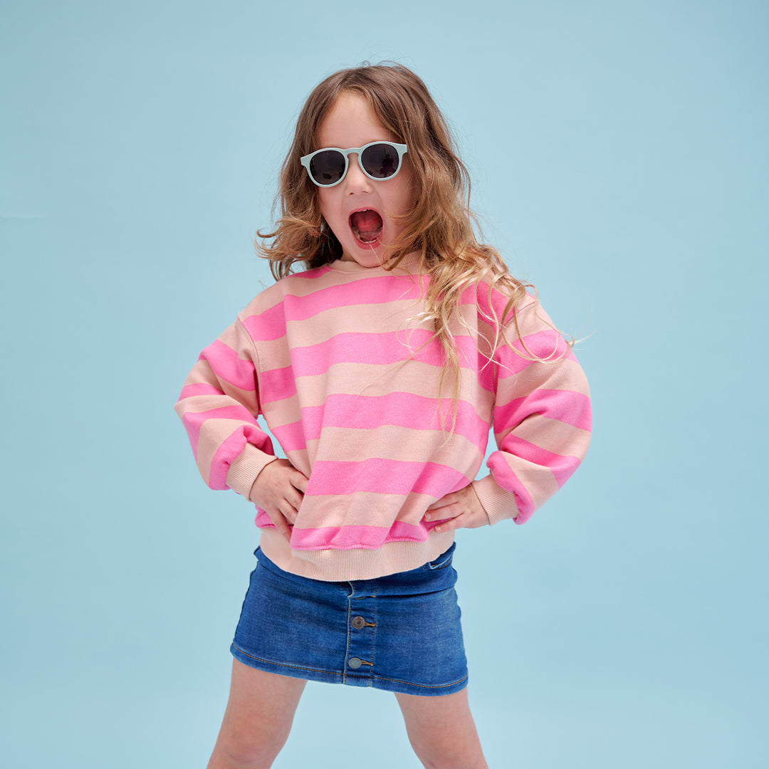 Child wearing a pink and beige striped sweater and sunglasses against a light blue background