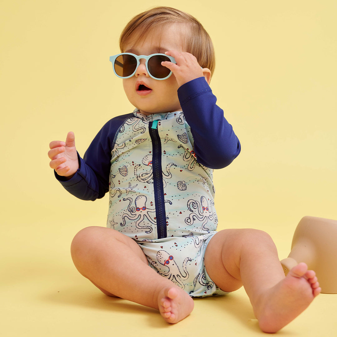 Baby wearing a patterned outfit and sunglasses on a yellow background