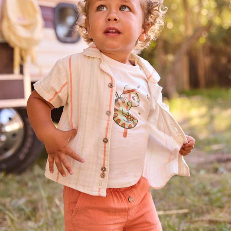 Child wearing a light-colored shirt with a number design and coral shorts outdoors.