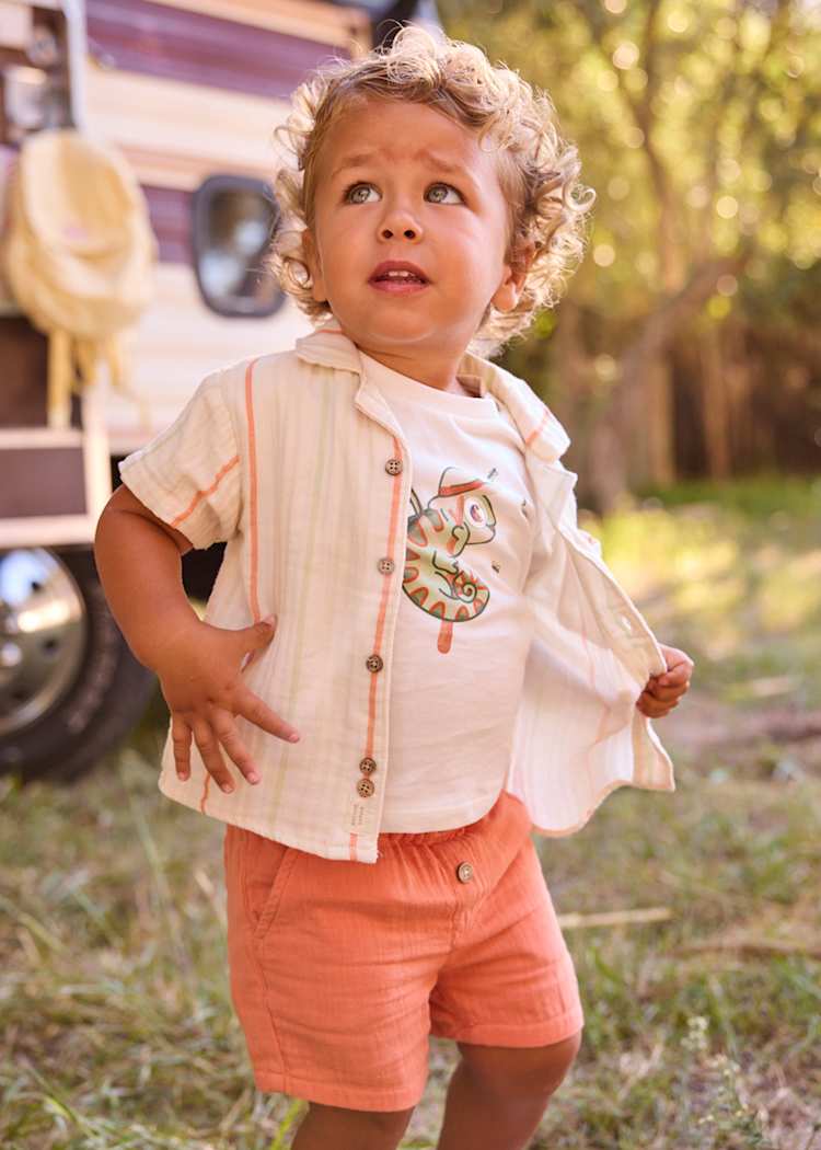 Child wearing a light-colored shirt with a number design and coral shorts outdoors.