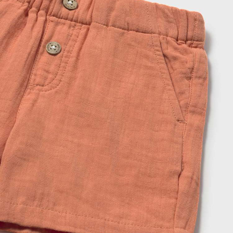 Close-up of terracotta shorts with button details on a light gray background
