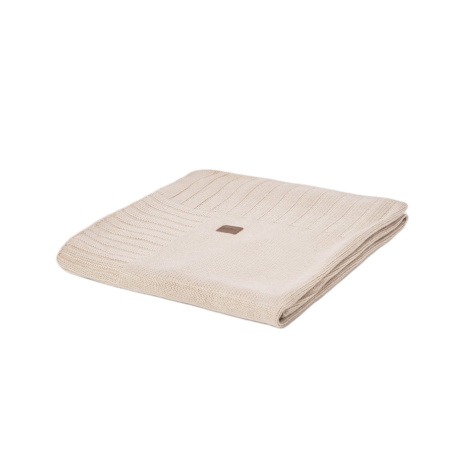 A folded cream-colored ribbed knit blanket with a small brown square brand tag, shown on a solid white background.