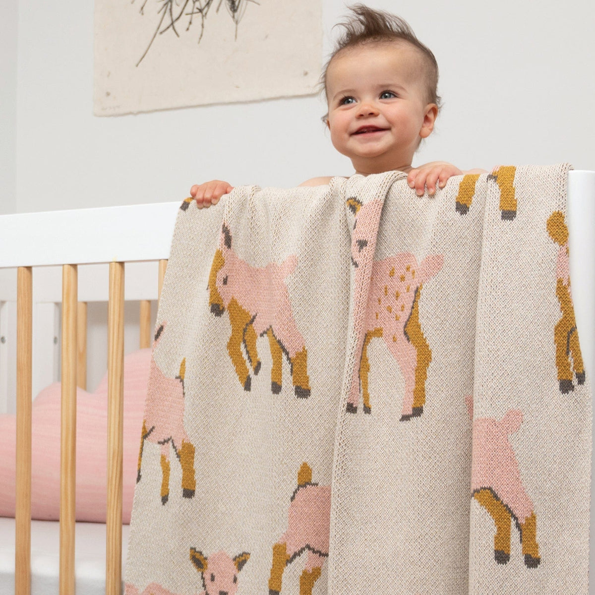 Child with a blanket featuring deer patterns in a crib