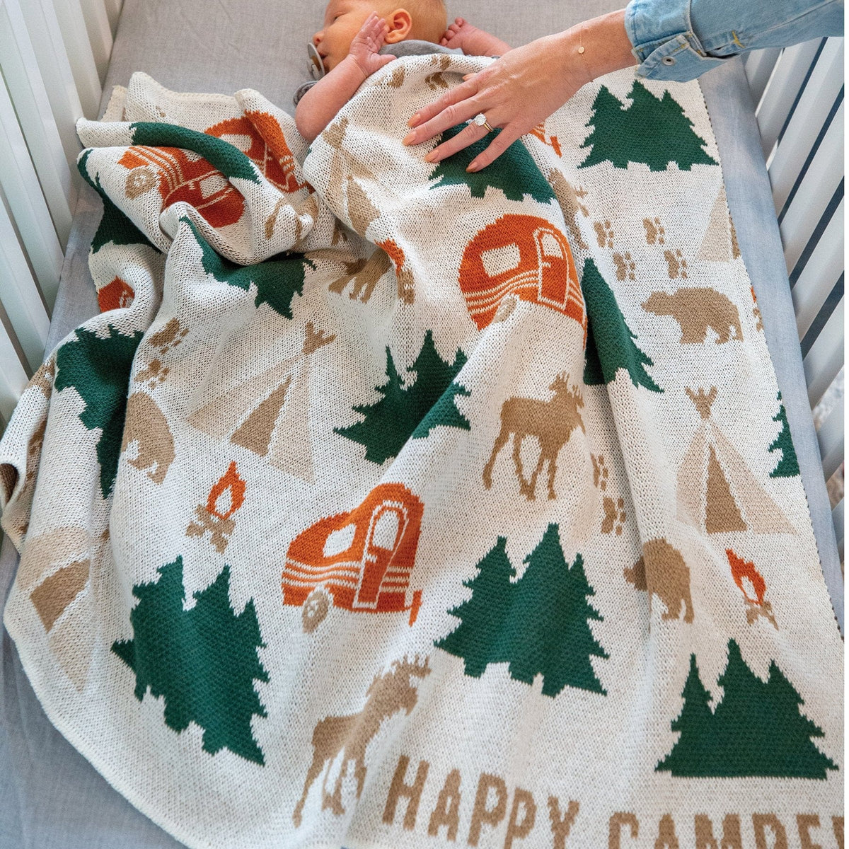 Baby wrapped in a 'Happy Camper' themed blanket in a crib