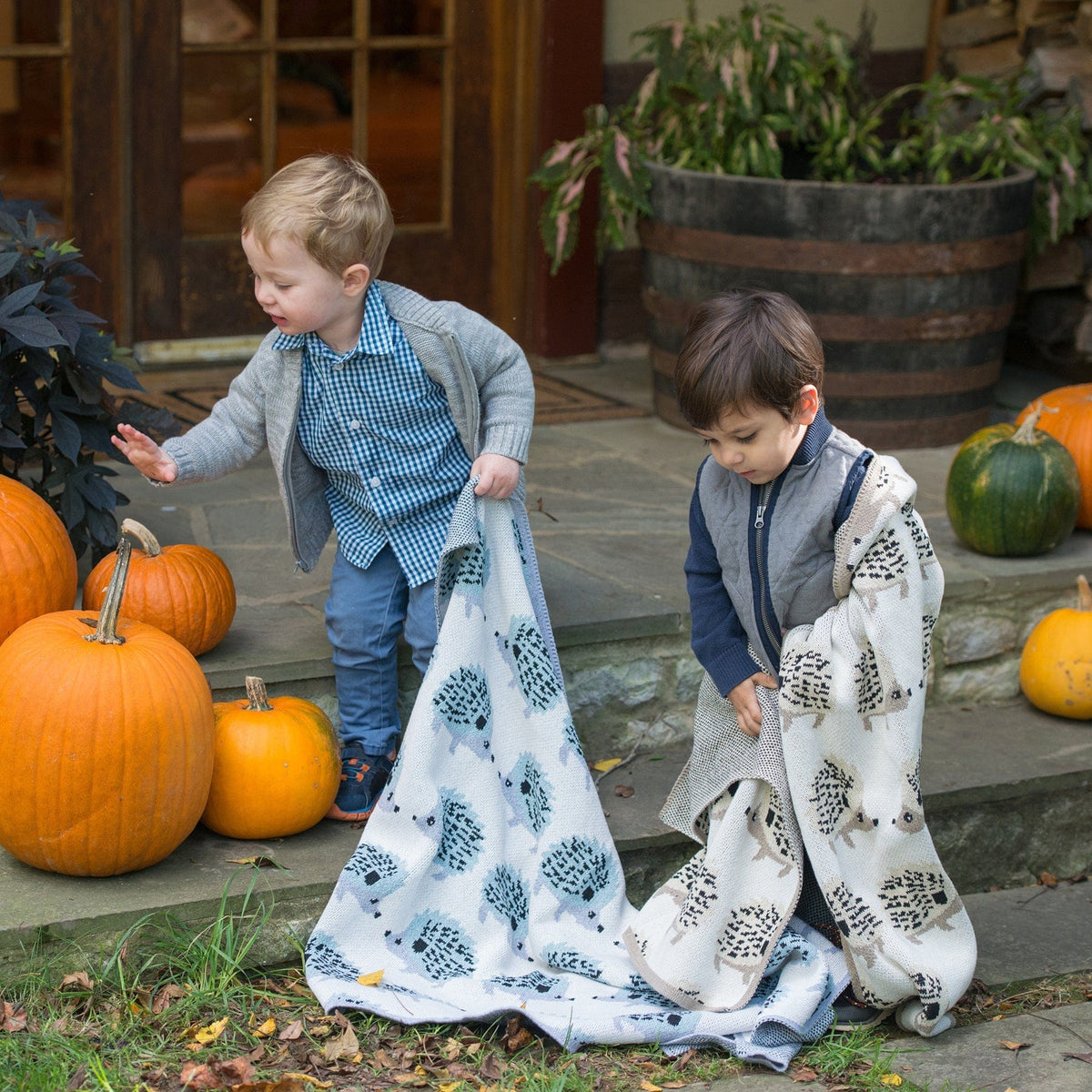 Two children playing with patterned cloths near pumpkins outdoors.