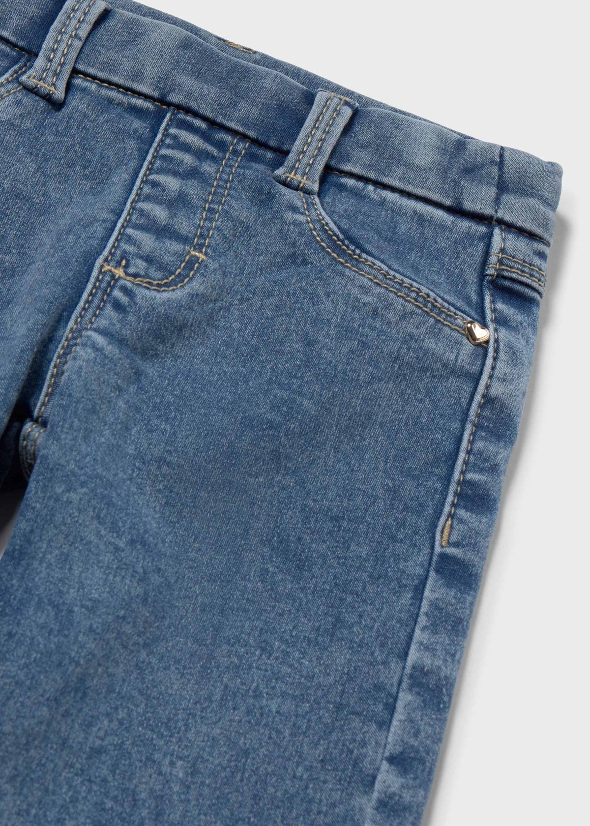 Close-up of blue denim jeans showing the waistband, belt loops, front pocket, and stitching details against a light gray background.