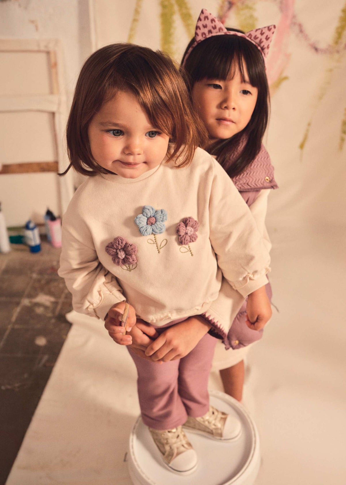 Two young girls in matching outfits with decorative elements on a neutral background