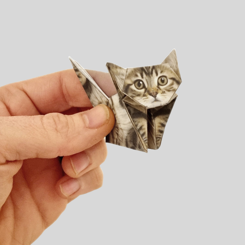 Hand holding a small origami cat on a light gray background