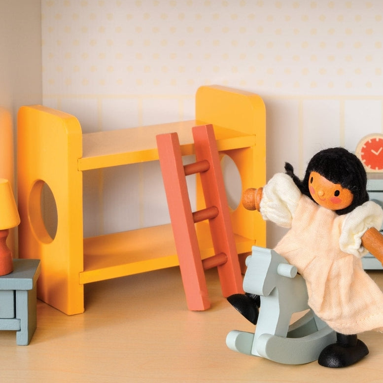 Wooden doll figure riding a light blue rocking horse in a miniature room with a yellow bunk bed, slide, chest of drawers, and bedside table with a lamp.