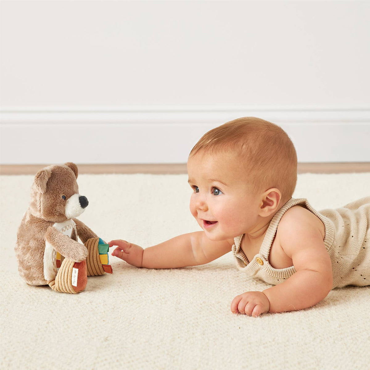 Baby lying on a white blanket with a teddy bear toy