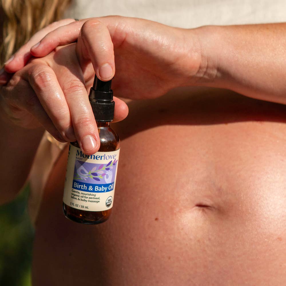 Person holding a bottle of Motherlove Birth & Baby Oil over a pregnant belly.