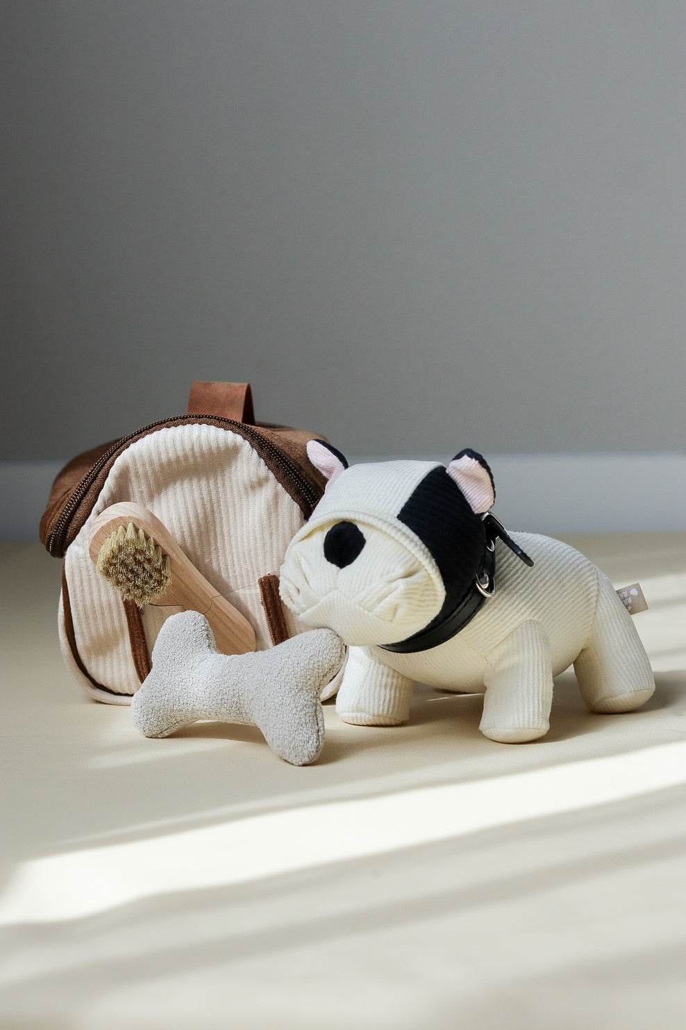 Stuffed dog toy with a bone and a doghouse on a light surface with a gray background