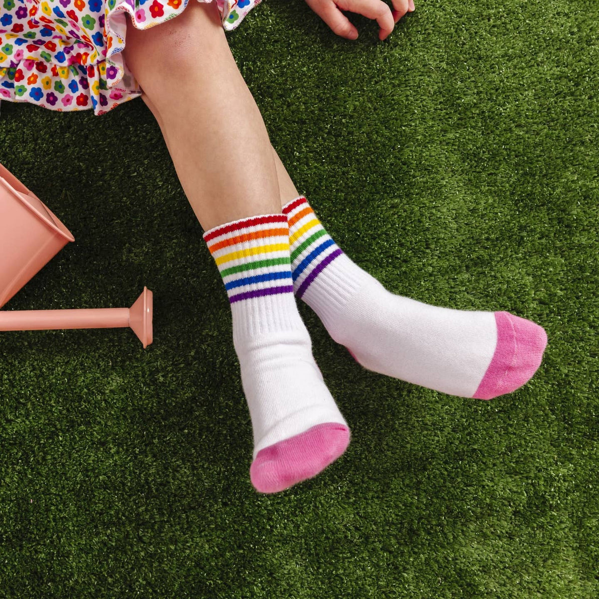 Child's legs wearing white socks with rainbow striped tops on a grassy surface.