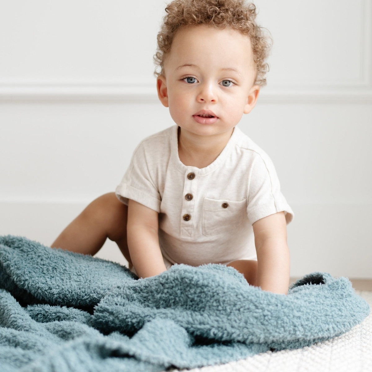 Child sitting on a bed with a blue blanket