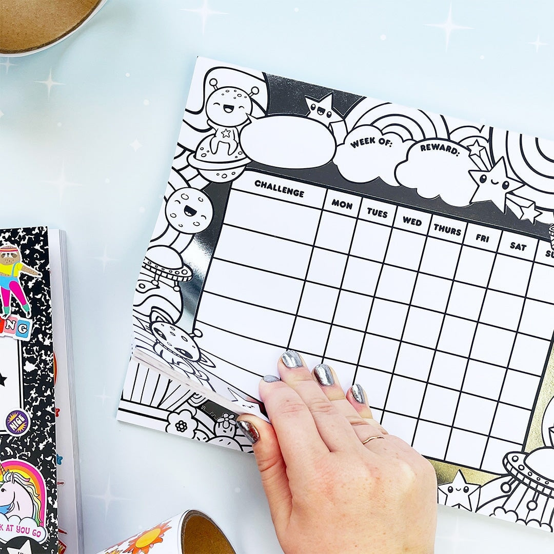 Hand holding a coloring page with a grid and decorative elements on a light blue surface.