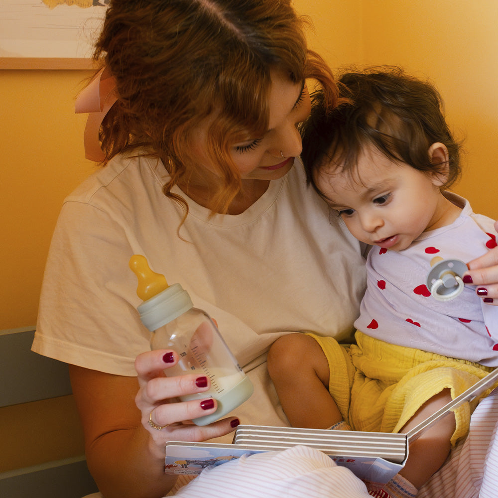Woman holding a baby and a bottle, with a yellow background