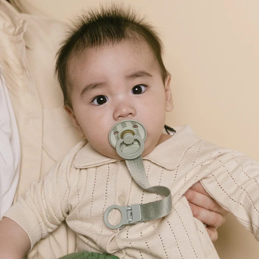Baby wearing a beige outfit with a pacifier held by an adult