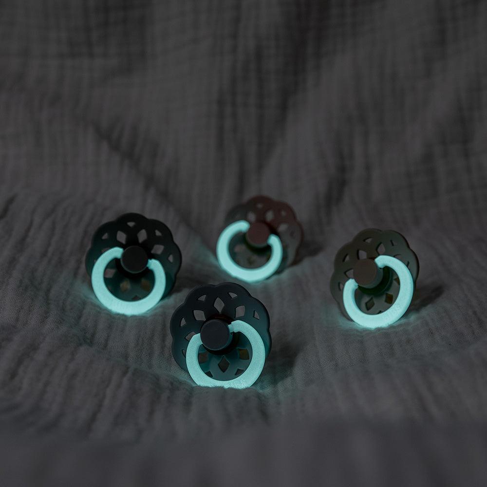 Four black and teal pacifiers on a textured dark surface