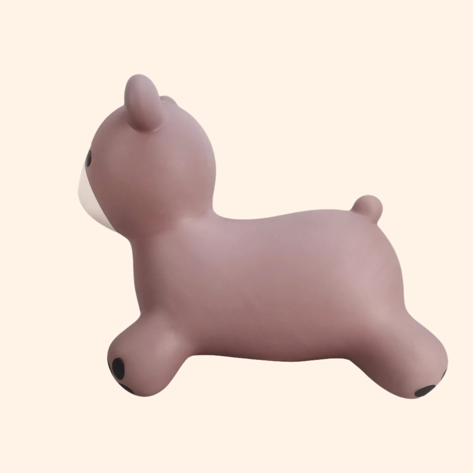 A small, soft silicone bunnie-shaped toy in a dusty mauve-pink color, featuring a white muzzle and small black paw pads, shown against a solid pale beige background.