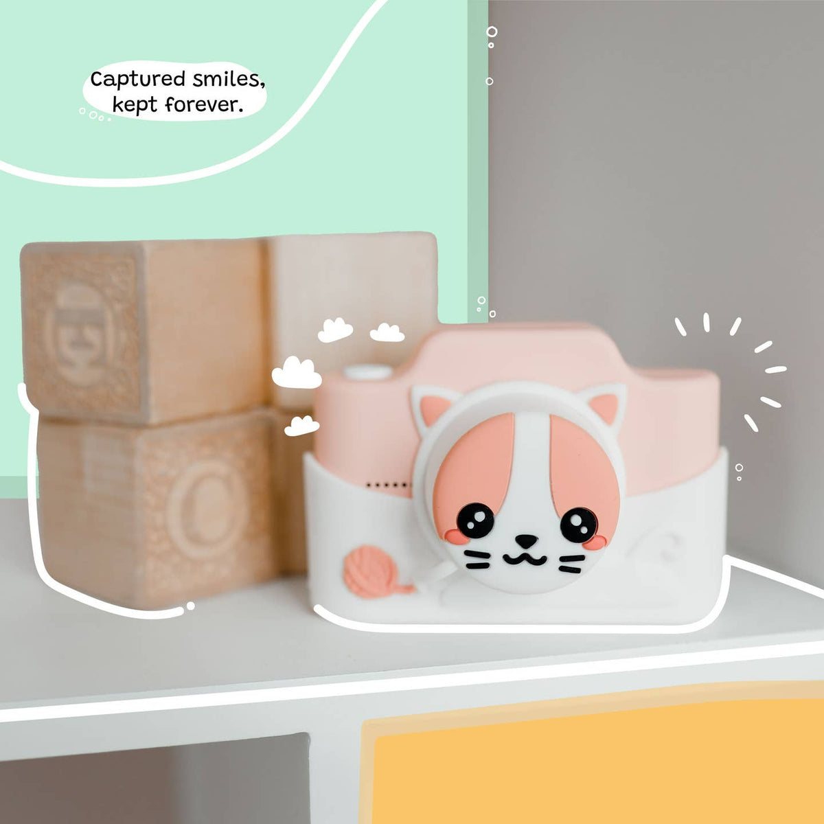 Pink camera-shaped container with a cat design on a shelf, surrounded by wooden blocks.