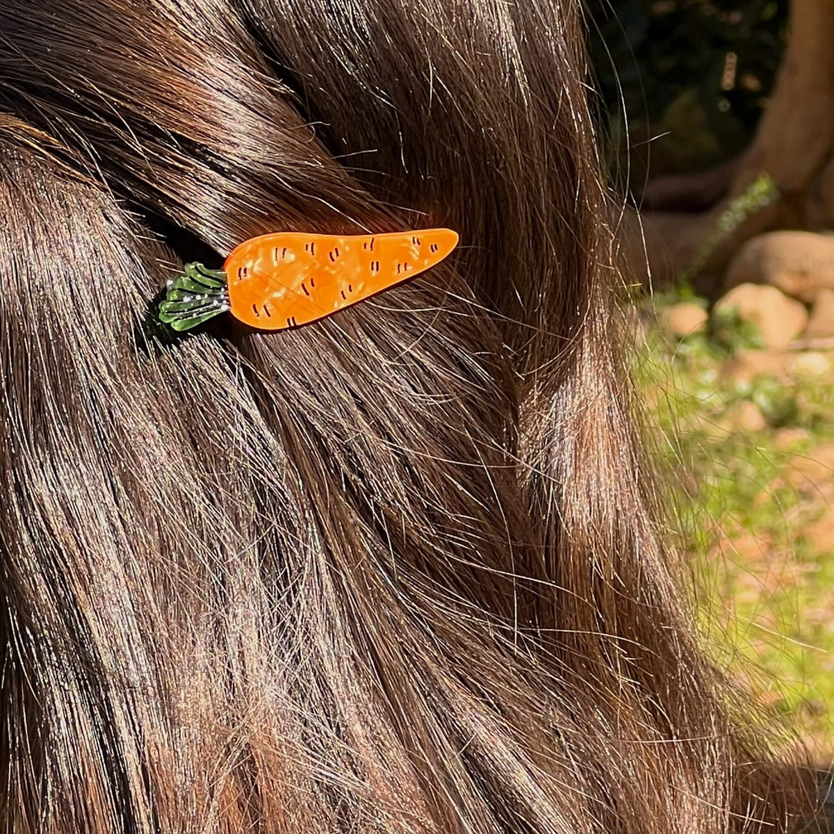 Carrot-shaped hair clip on a person's hair with a natural outdoor background