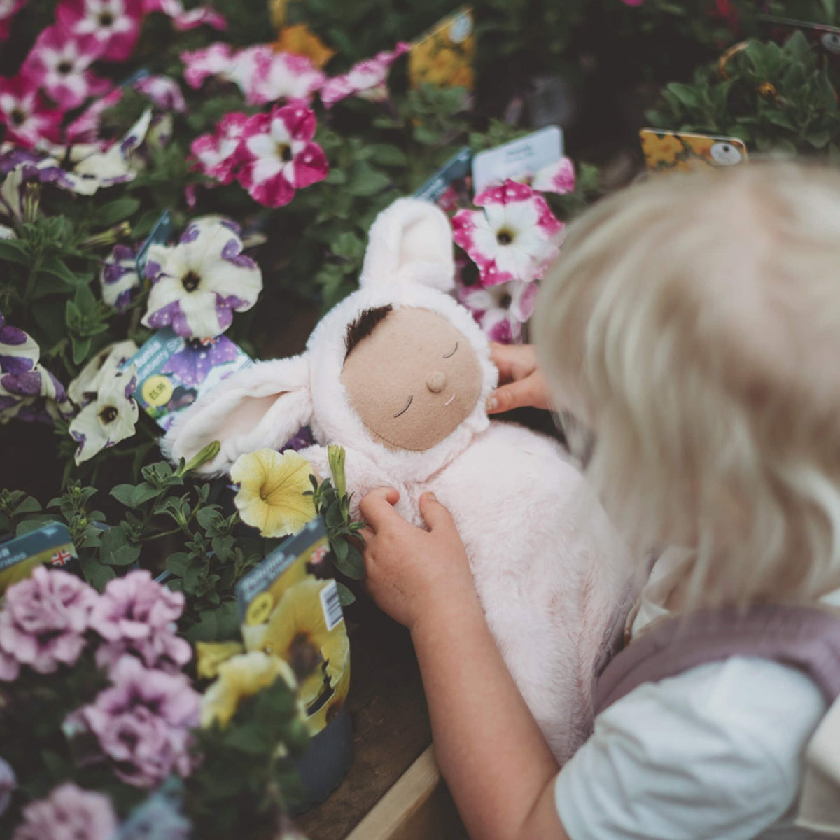Child holding a plush toy among flowers