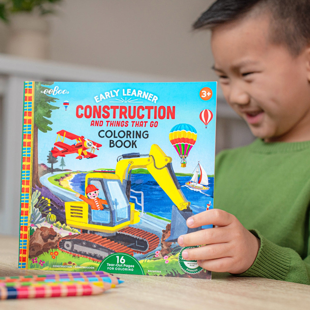 Child holding a coloring book titled 'Construction and Things That Go' by eeBoo.