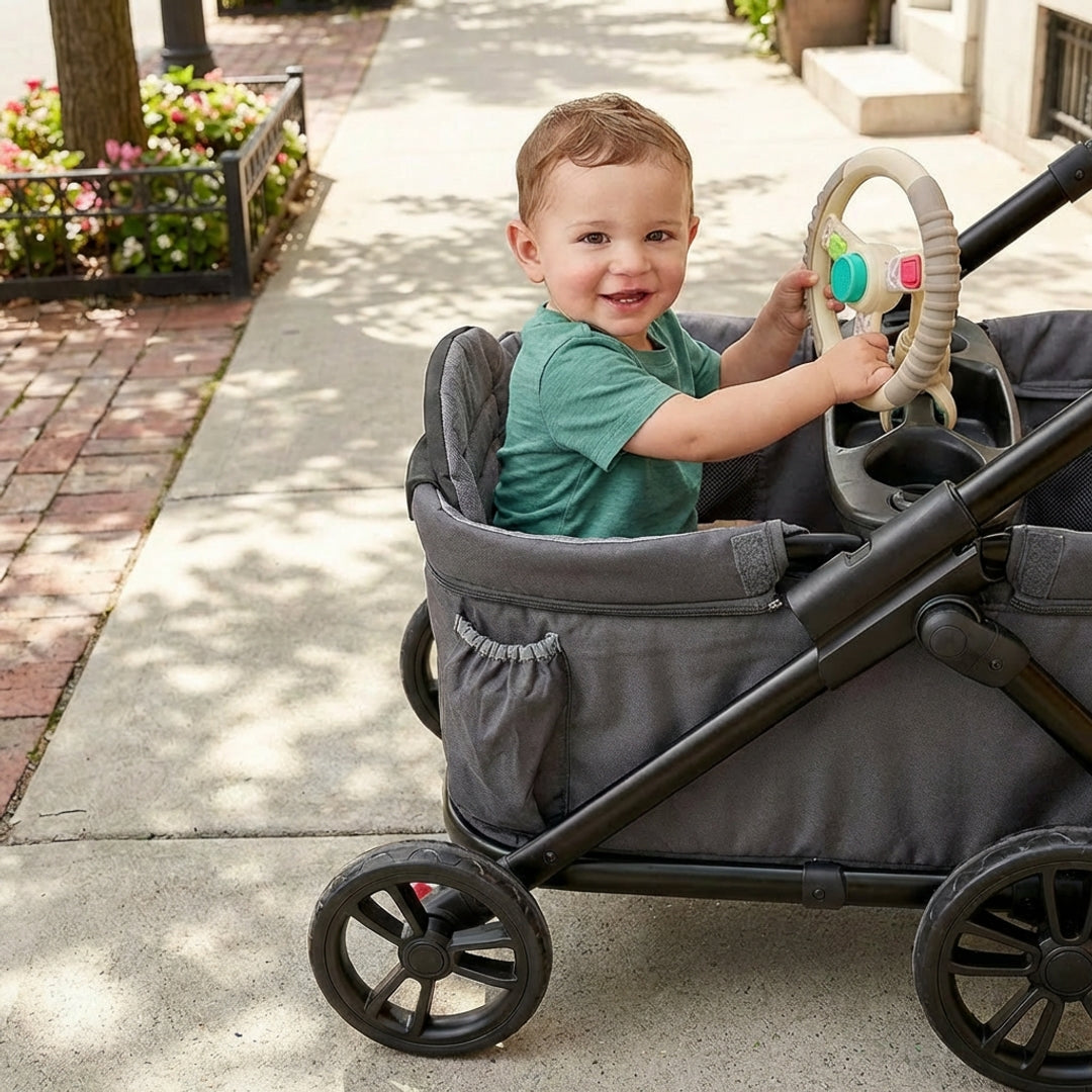 Child playing with a toy steering wheel in a stroller on a sidewalk.