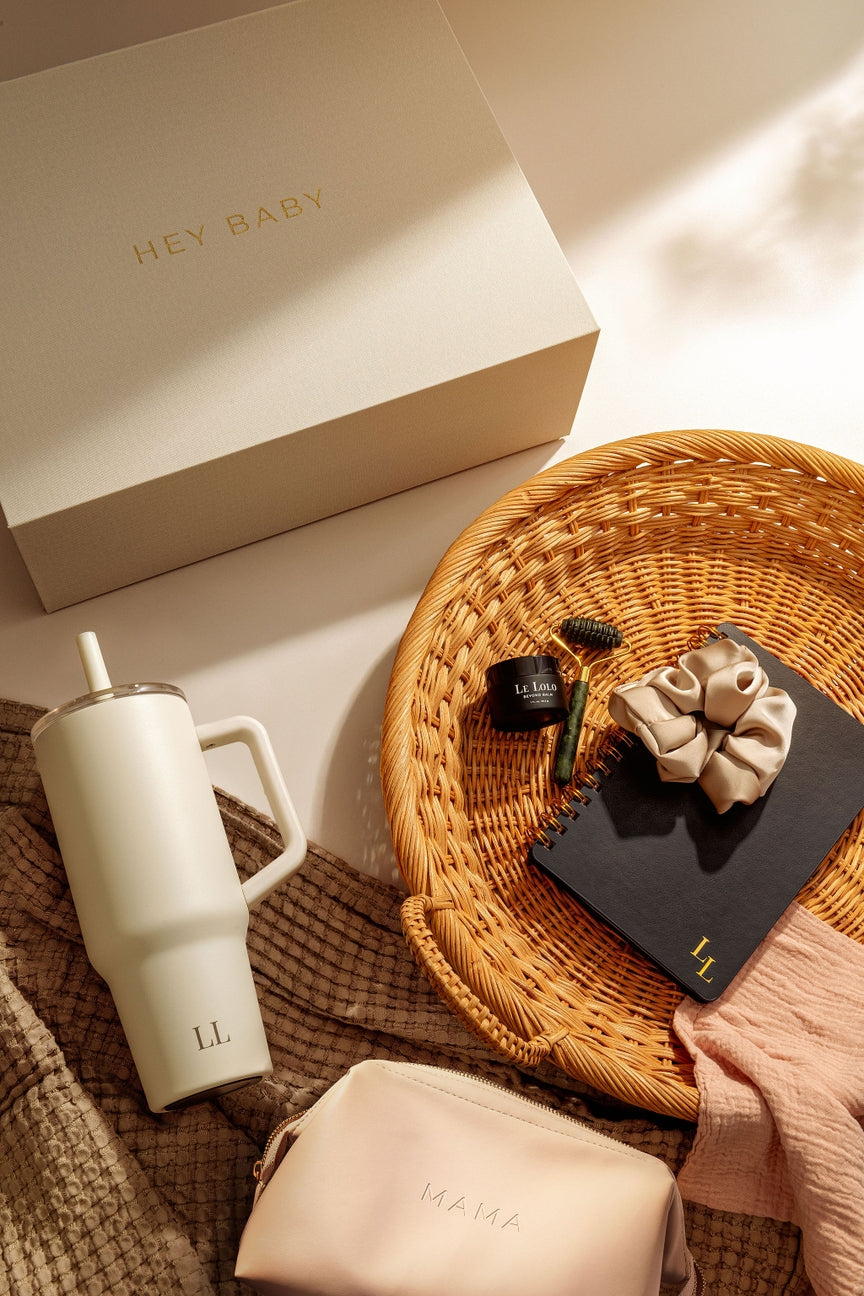 White tumbler, beige pouch, and decorative items on a textured surface with 'HEY BABY' box.