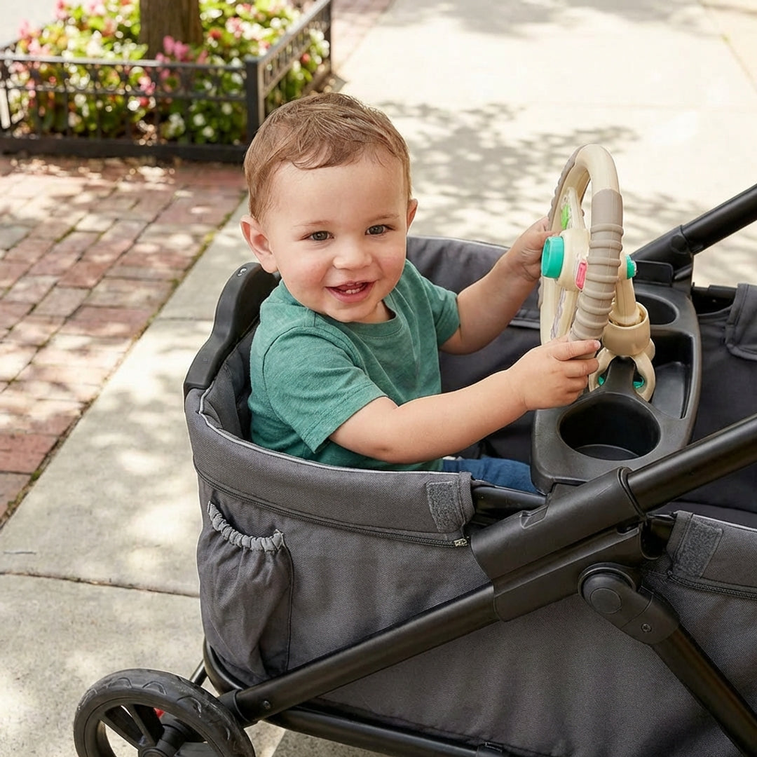 Child playing with a toy steering wheel in a stroller on a sidewalk.