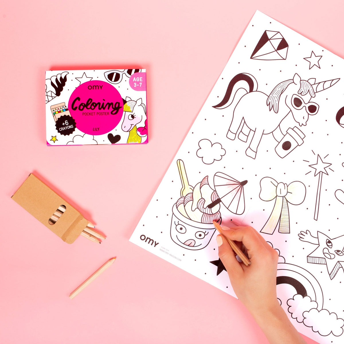 Pencil held by hand coloring a book on a pink background