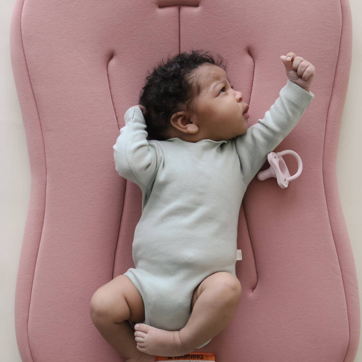 Baby lying on a pink cushion with a pacifier nearby