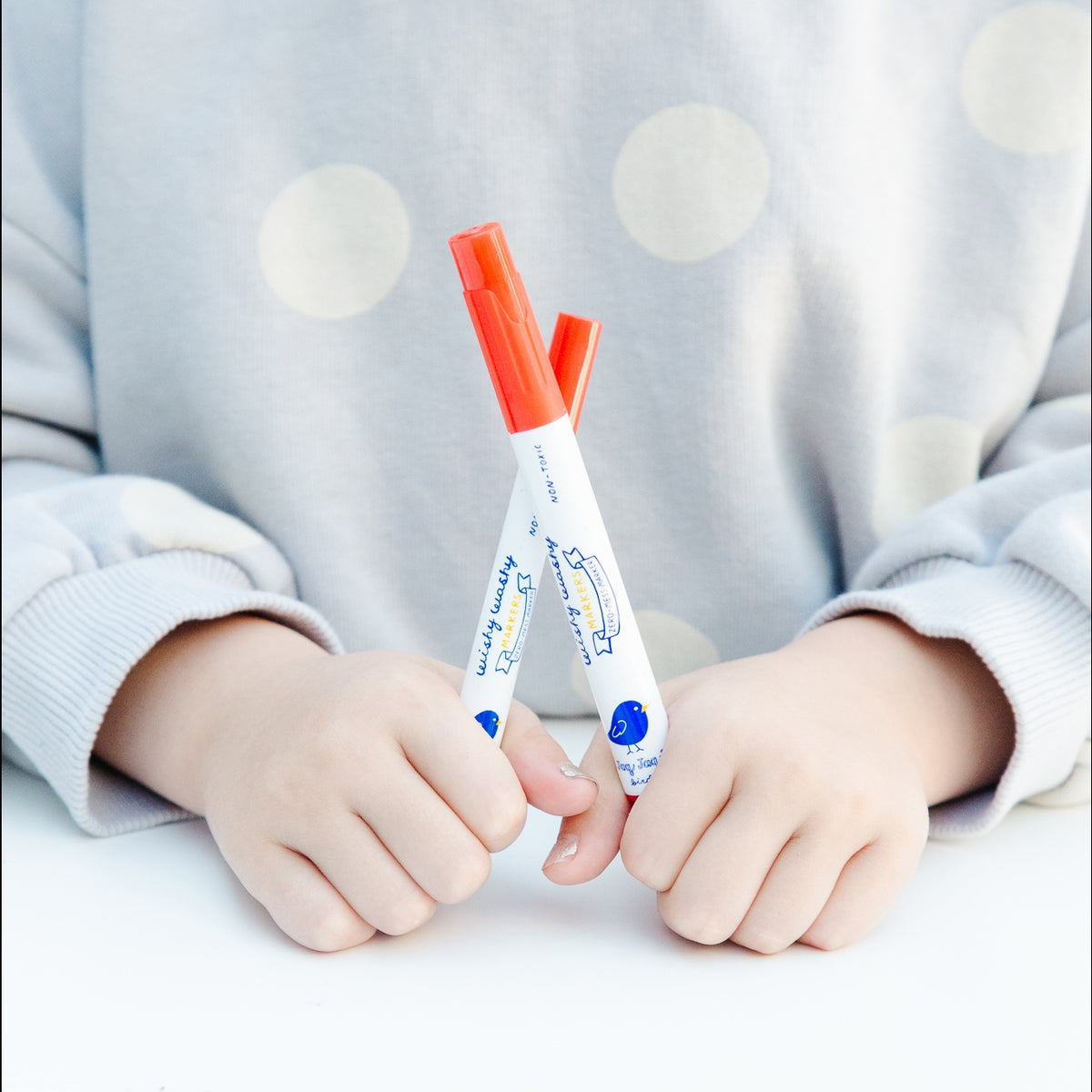 Two markers held by a child against a light gray background