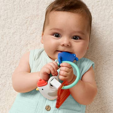 Baby holding a colorful teething toy against a neutral background