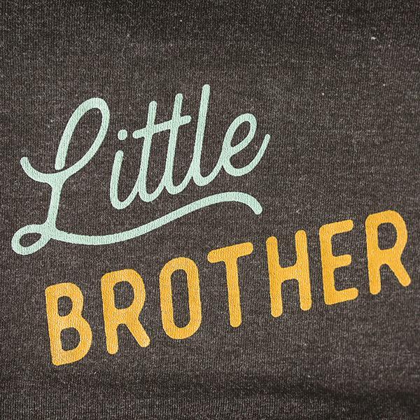 Text 'Little Brother' on a dark fabric background