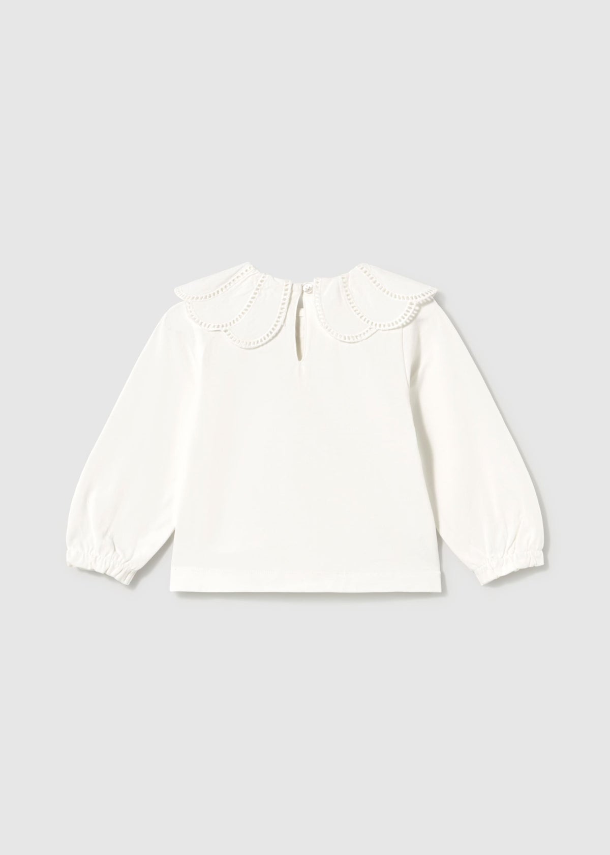 An off-white long-sleeve blouse for a toddler, featuring a decorative ruffled collar with embroidered details and elasticized cuffs, shown flat on a light gray background.