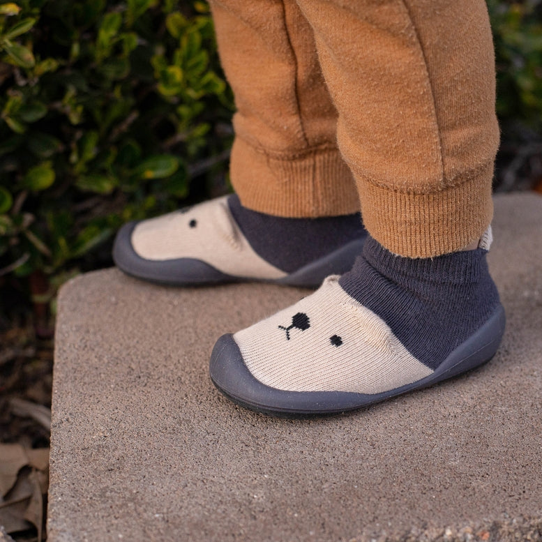 Children's shoes with navy socks worn, standing on a stone surface with greenery in the background