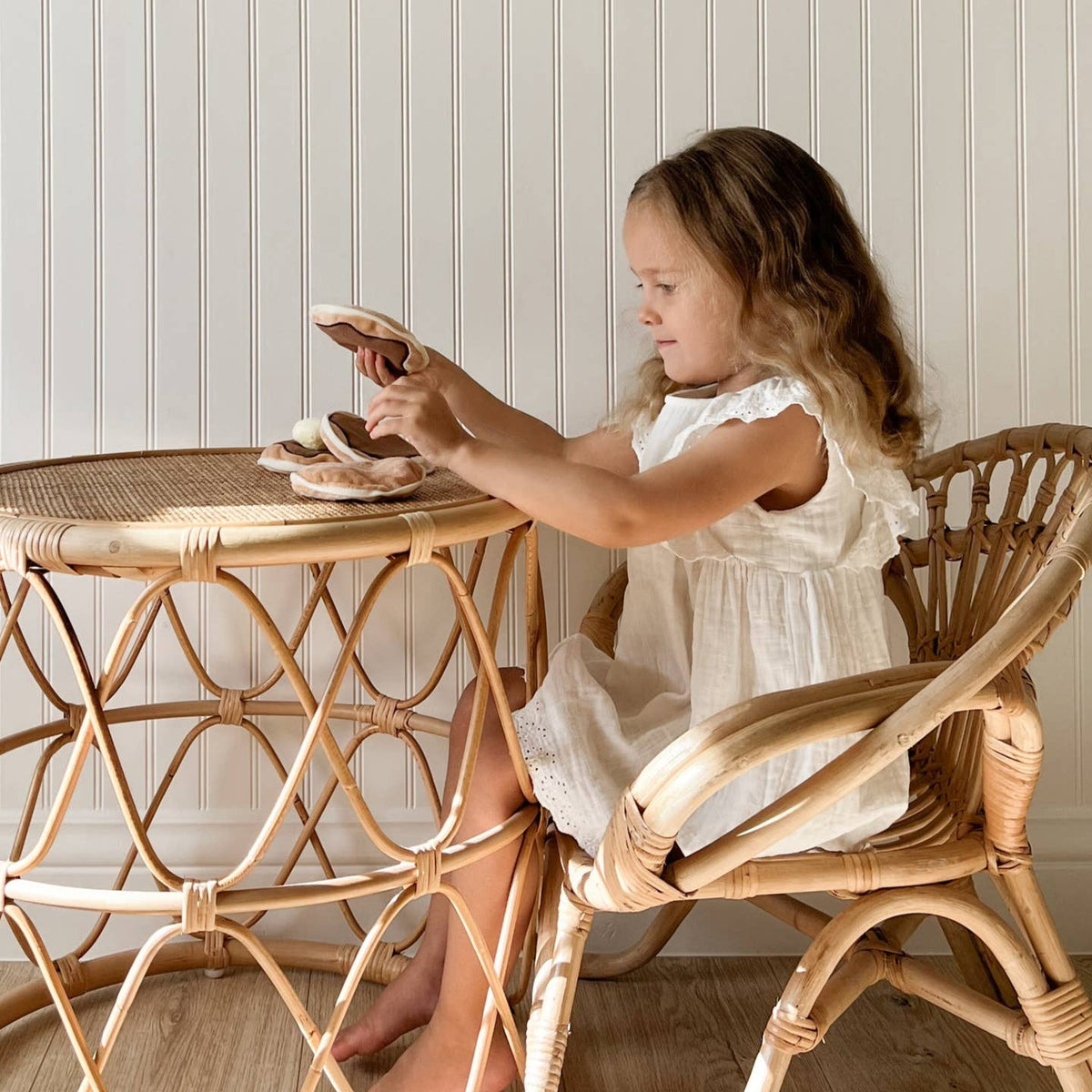 Young girl sitting at a wicker table with a wicker chair, playing with toys.